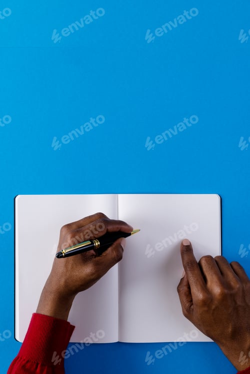 Preview: Hands of biracial man holding pen and writing in notebook with copy space on blue background
