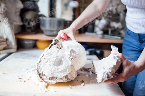 Preview: Female artist carefully sculpting a plaster skull model in a creative studio