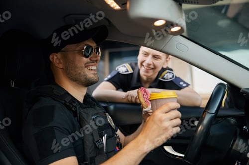 Preview: Smiling patrol police officers diverse team sitting in car having coffee break time at work