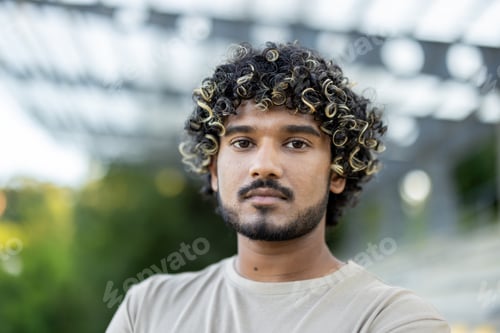 Preview: Close-up portrait of a young calm and serious man, looking at the camera, walking outside in the