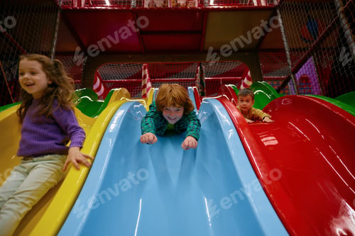 Preview: Happy children riding slide together at indoor play center