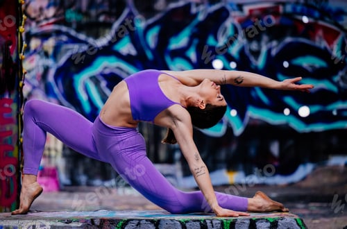 Preview: Woman in purple athletic wear performs a yoga pose against a vibrant graffiti background. USA