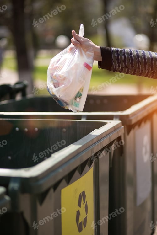 Preview: Hand with a bag of plastic garbage over containers for separation and sorting