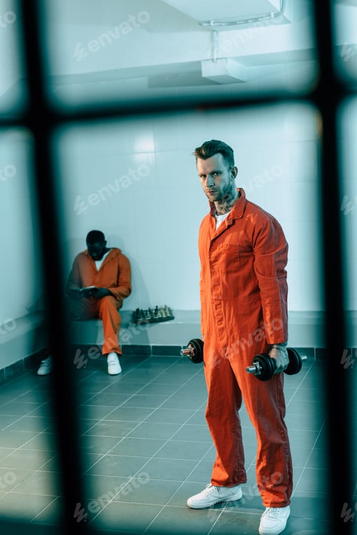 Preview: prisoner training with dumbbells in prison room and looking at camera