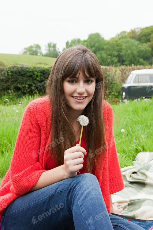 Preview: Young woman enjoying a moment with a dandelion in a grassy field.