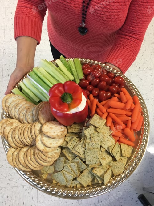 Preview: Woman in salmon colored sweater holding a healthy but tasty office party tray