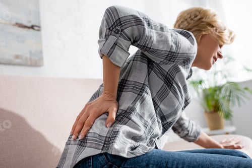 Preview: selective focus of mature woman suffering from back pain while sitting on sofa