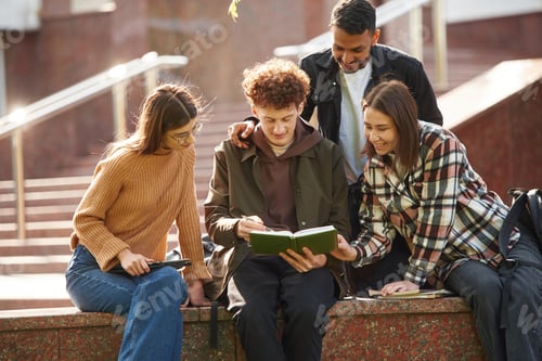 Preview: Sitting, reading educational material. Four young students in casual clothes are together outdoors