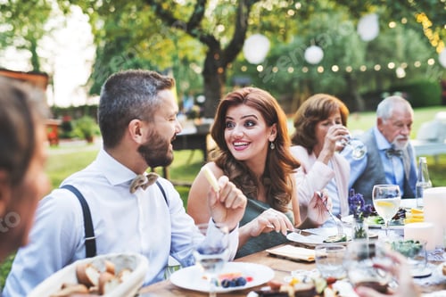 Preview: Guests eating at the wedding reception outside in the backyard.
