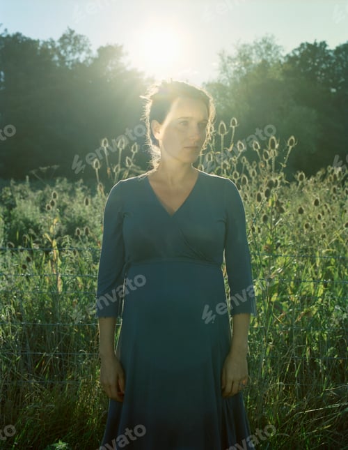 Preview: Backlit portrait of mid adult woman gazing from long grass