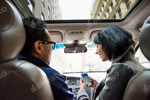 Preview: A young woman and young man in a car looking at a map on the display of a cellphone, seen from the