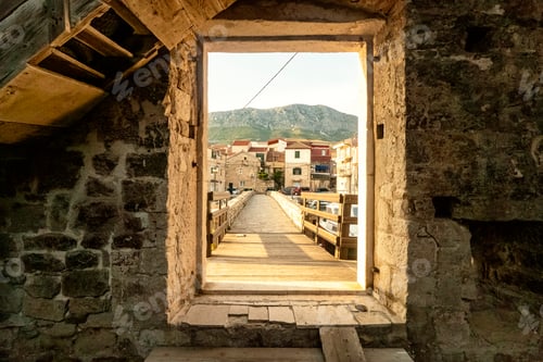 Preview: Stone window framing a view of an old bridge and historical buildings against a backdrop