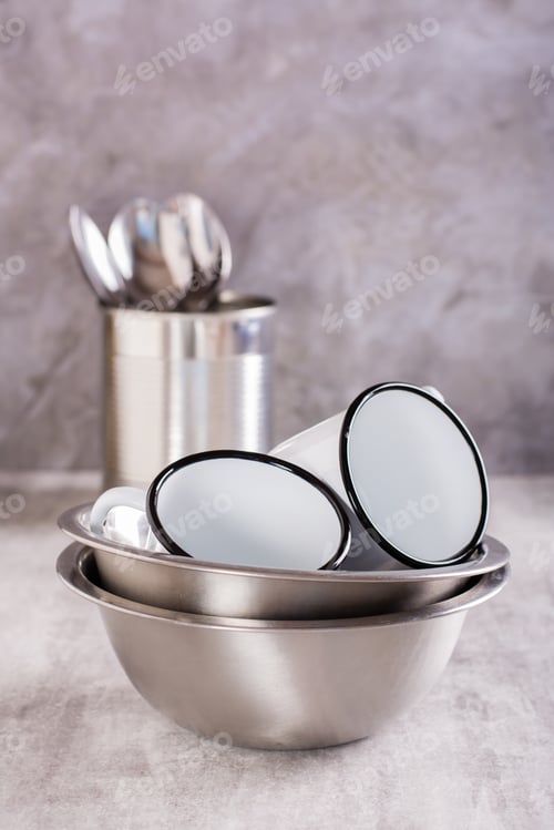 Preview: A set of metal utensils from bowls, enameled mugs and spoons on a vertical gray background