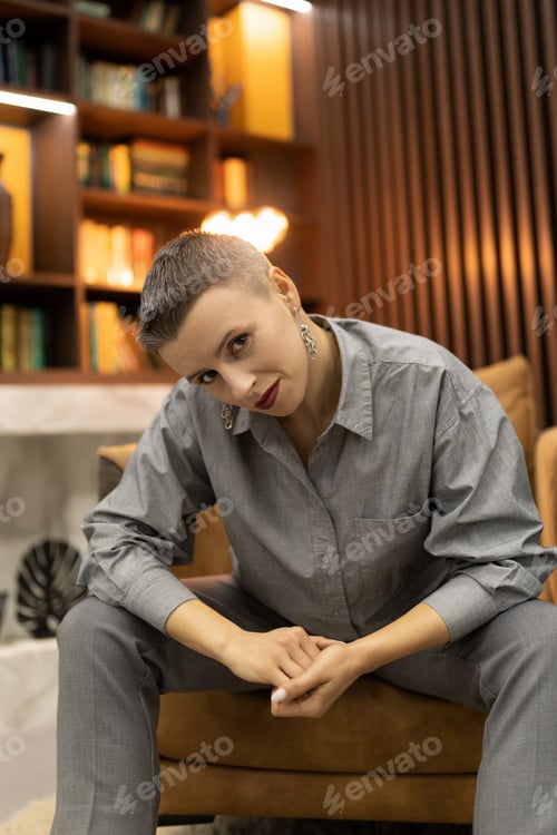 Preview: Caucasian style a woman with a short haircut sits in an easy chair on the background of the library