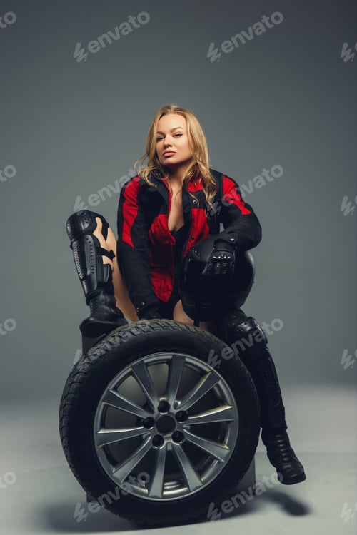 Preview: Female in motorcycle uniform posing with car wheel.