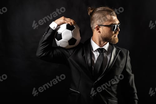 Preview: Businessman in suit holds soccer ball with confidence in a dark studio
