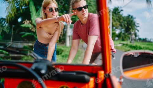 Vista previa: Male and female looking through map on car hood