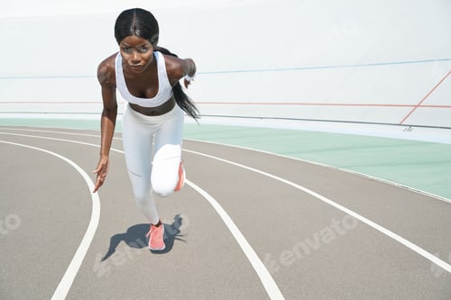 Preview: Beautiful young African woman in sports clothing running on track outdoors