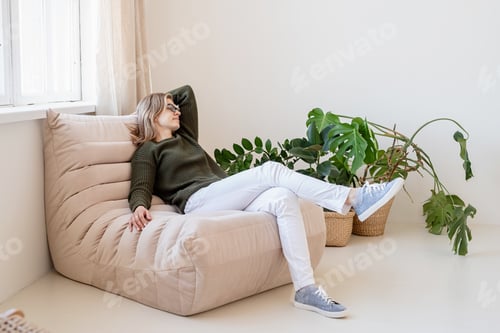 Preview: Attractive young woman sitting on the chair in light and airy interior with plants