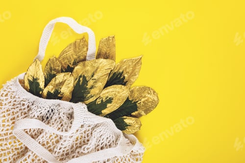 Preview: Reusable shopping net bag with green and golden leaves on yellow fall autumn background. Top view of