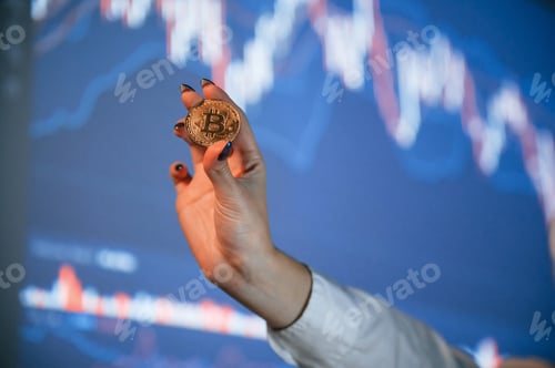 Preview: Close up view of woman's hand that holding physical bitcoin against background with graphs