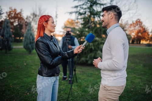 Preview: Female journalist interviewing businessman in a park with cameraman filming