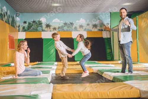 Preview: happy parents with adorable little kids holding hands and jumping in entertainment center