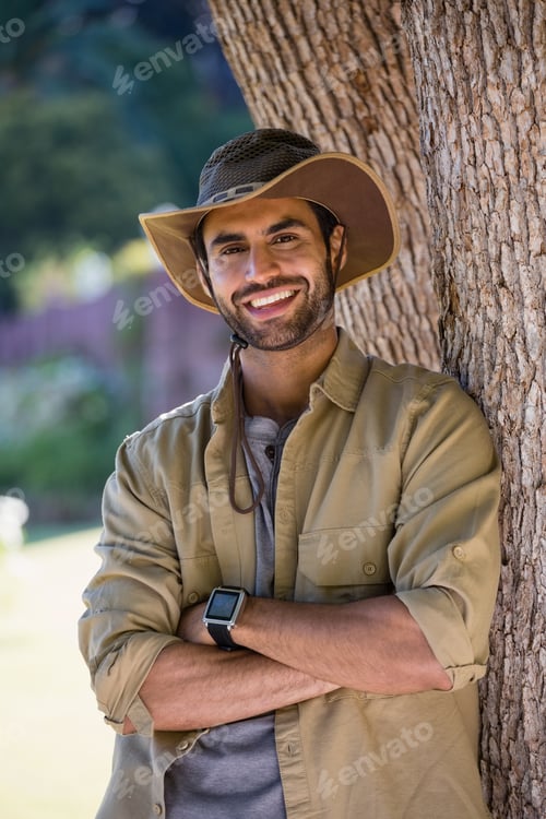 Preview: Smiling man standing with arms crossed near tree trunk