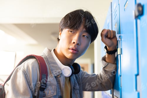Preview: Opening locker, asian teenage boy with headphones looking away in school hallway