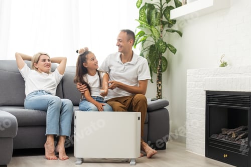 Preview: Electric heater at home. Young family warms his frozen hands near a heating radiator
