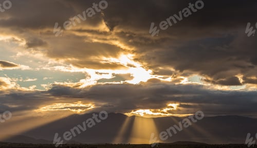 Preview: Stormy heavy clouds above fields and mountains with sunrays passing through.