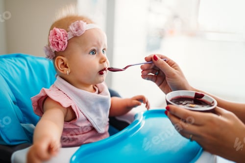Preview: Mother feeding baby with spoon indoors