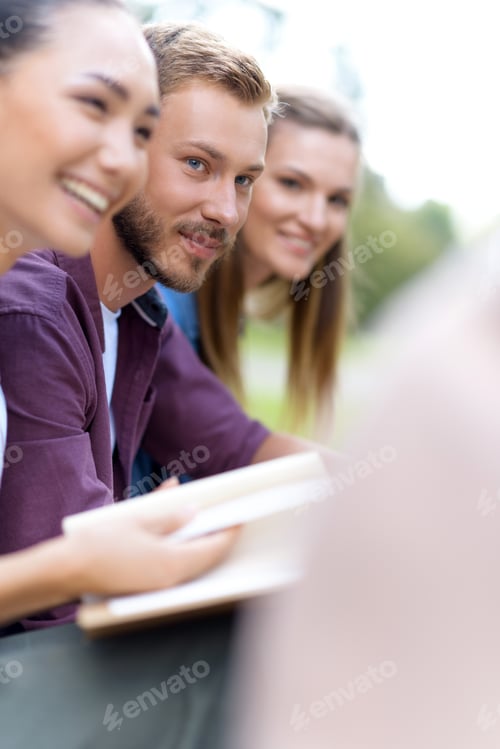 Preview: cropped shot of smiling young multiethnic students reading book and looking at friend