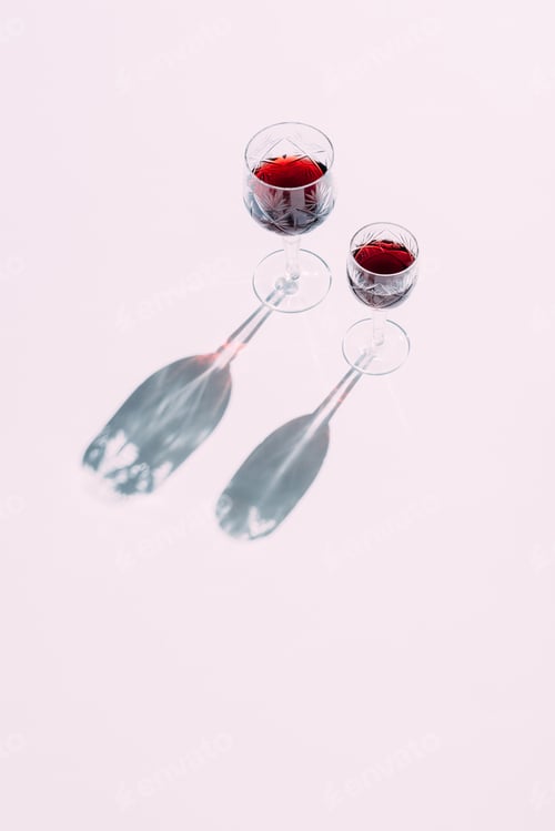 Preview: Two crystal glasses of red wine casting shadows on pink tabletop