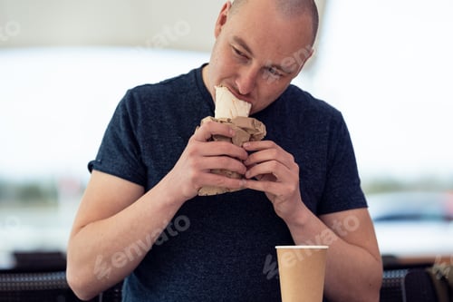 Preview: White man eating shawarma. Eco cup of tea or coffee.