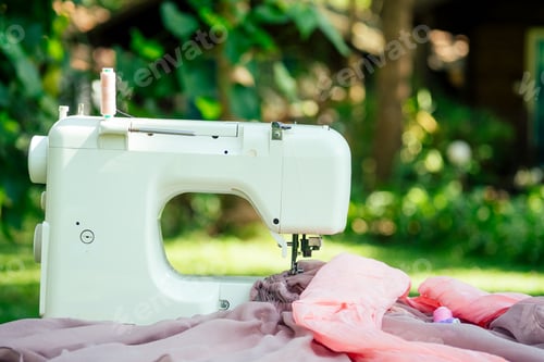 Preview: sewing machine outdoors in summer park against the background of the wooden house