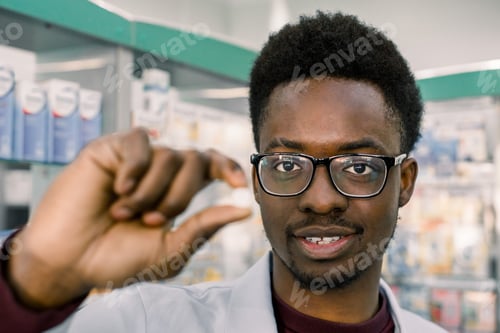 Preview: Young smiling African-american Doctor pharmacist man holding white tablet pill in the hand, close-up