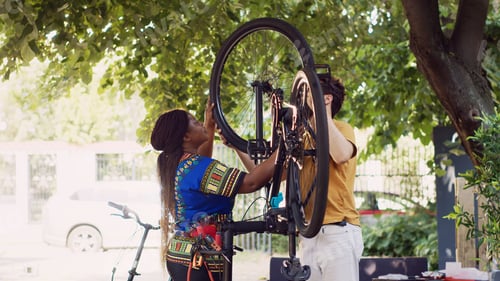 Preview: Multiethnic couple fastens bicycle wheel
