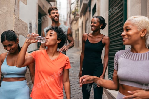 Preview: Group of sporty friends walking and drinking water in the city after training