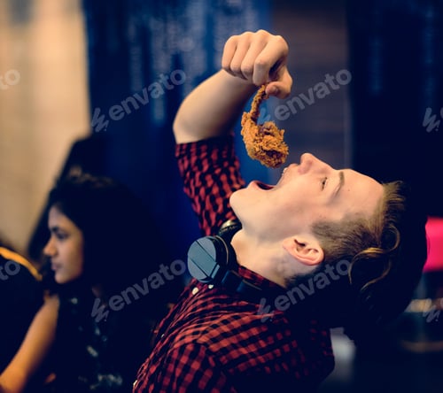 Preview: Close up of teenage boy eating fried chicken with his friends