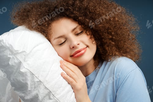 Preview: Closeup smiling young woman with curly hair sleeping on pillow, holding, with closed eyes