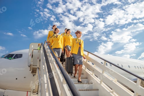 Preview: Cheerful stewardesses walking down airplane stairs under cloudy sky