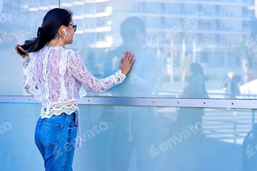 Preview: Smiling Asian girl listening to music with headphones is reflected in the glass on the street.