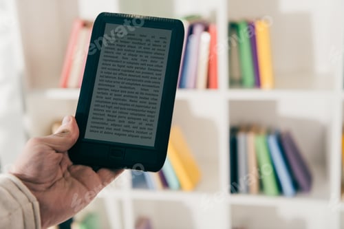 Preview: cropped view of man holding e-book in hand near bokkshelf