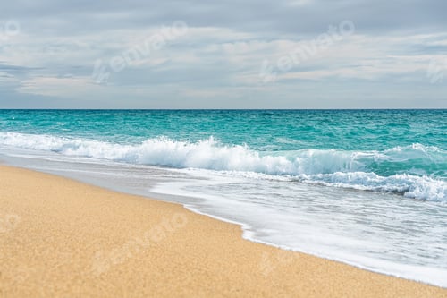Visualização: Ondas azul-turquesa do mar atingem suavemente a costa em uma praia de areia dourada sob céu nublado