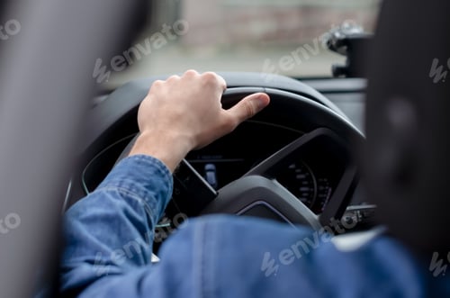 Preview: The hand of a young man on the steering wheel of a car, view from the back.