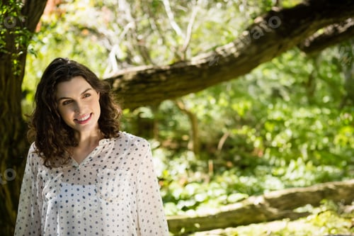 Preview: Woman wearing polka dot blouse leaning against moss-covered tree trunk in sunlit forest, copy space