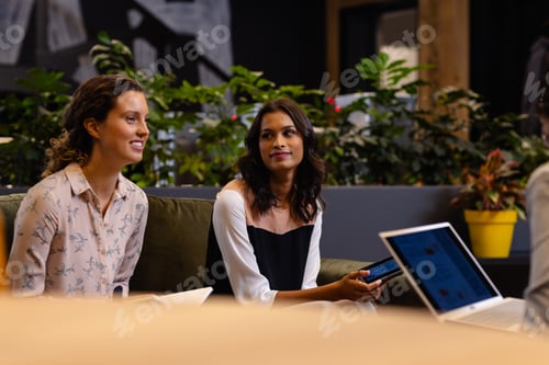 Preview: Diverse happy female colleagues in discussion using laptop in casual office meeting