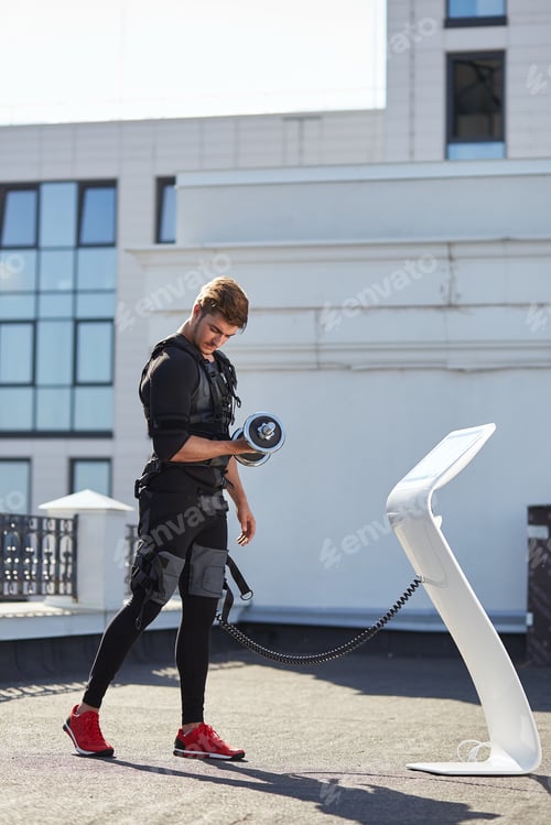 Preview: fit strong man connected to the EMS device is working out outdoors