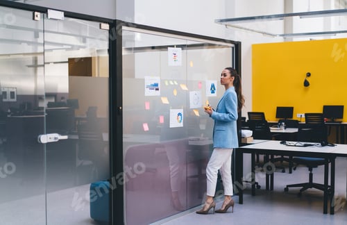 Preview: Businesswoman standing by glass wall with sticky notes in office